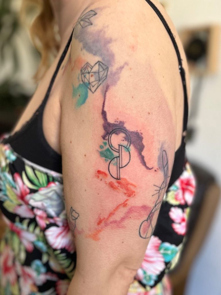 Abstraktes Watercolor Tattoo mit Farbe, feinen Linien und Organspendesymbol am Oberarm