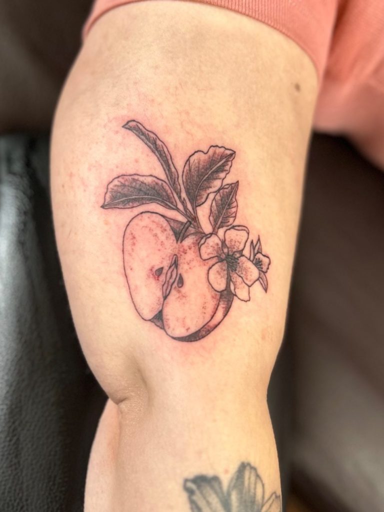 Botanisches Fineline Tattoo mit Apfel, Blüte und feinen Blättern am Oberarm