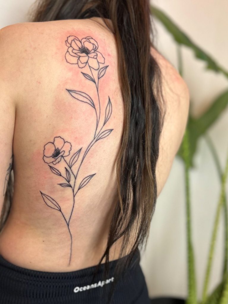 Florales Fineline Tattoo mit zwei feinen Blumen und langen Stielen am Rücken