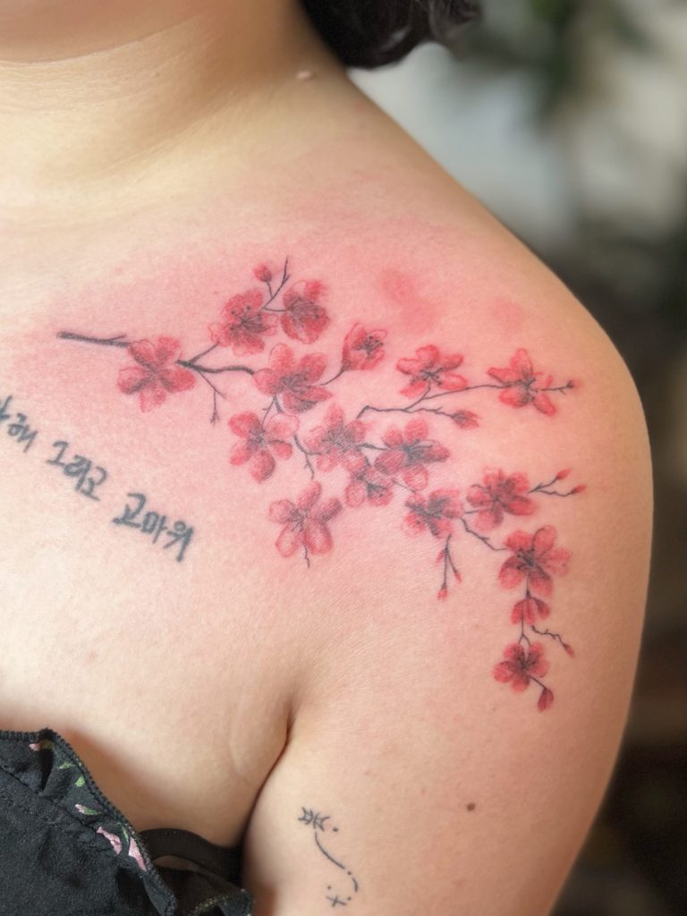 Kirschblüten Tattoo in Rot und Rosa mit feinen schwarzen Linien auf der Schulter