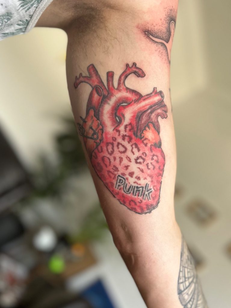 Anatomisches Herz Tattoo in Rot mit illustrativen Details und Schriftzug am Unterarm