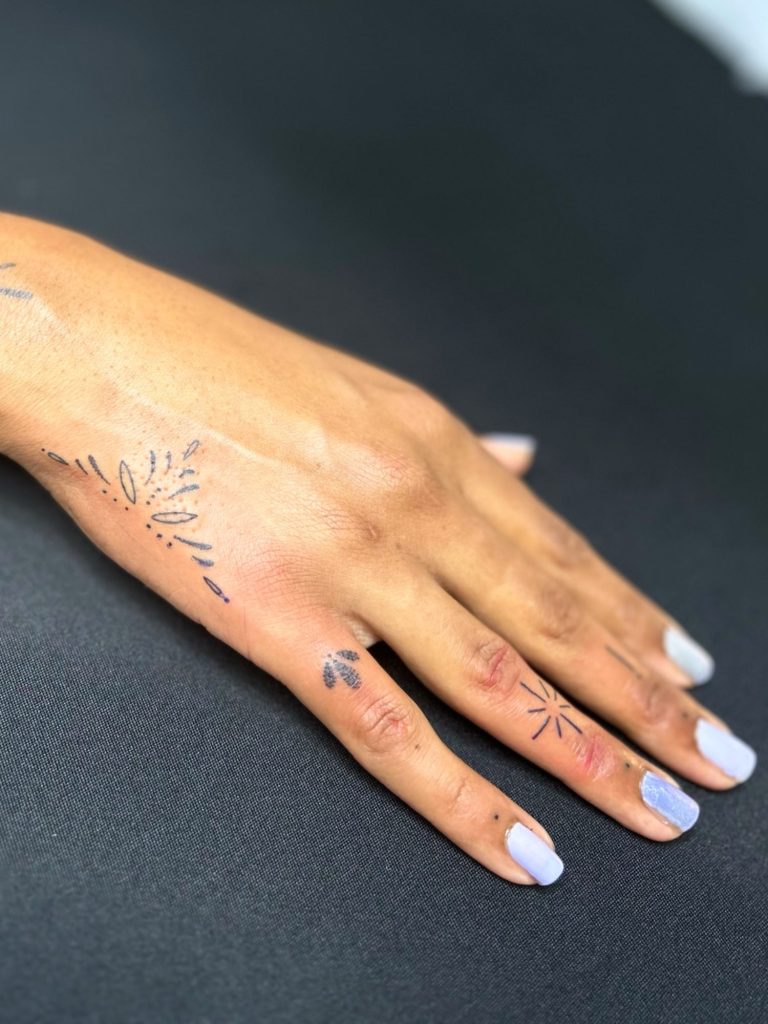 Minimalistische Fineline Tattoos mit kleinen Symbolen und ornamentalen Details an Hand und Fingern